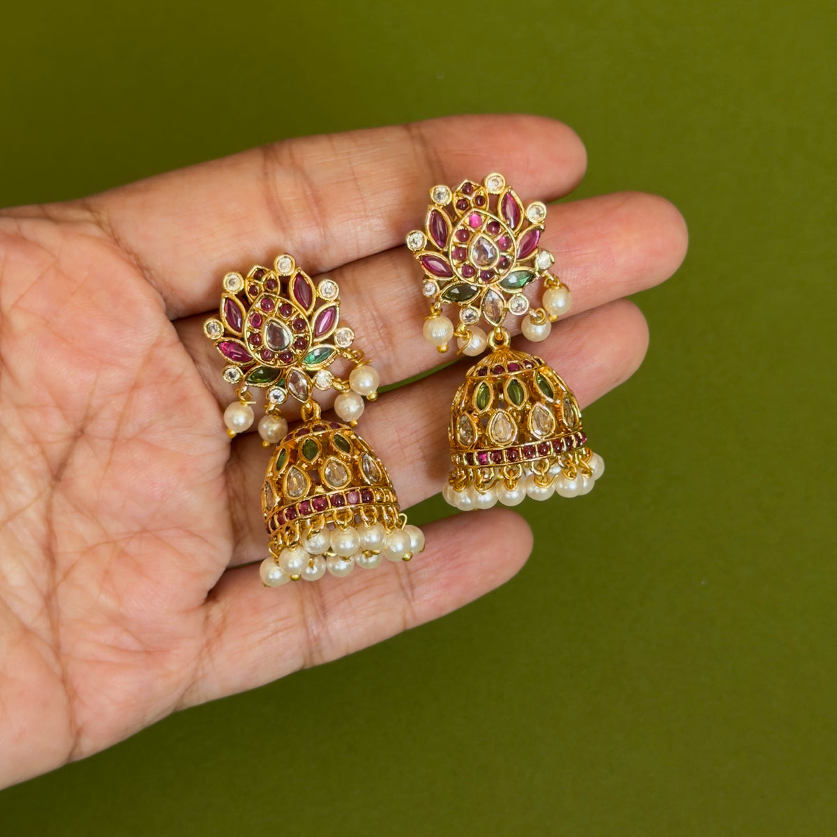 Gold-tone multicolour jhumka earrings with pearl-like drops held in a hand