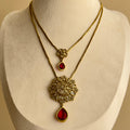 Layered gold-tone necklace with ornate pendant and red teardrop accents on display bust